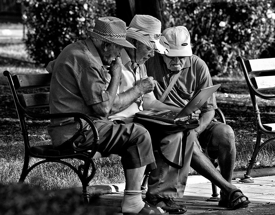 Three elderly men surfing the web while in the park